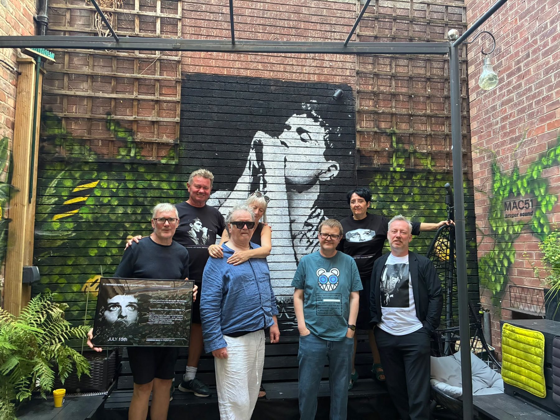 A group gathered in the Proper Sound courtyard in front of the Ian Curtis mural