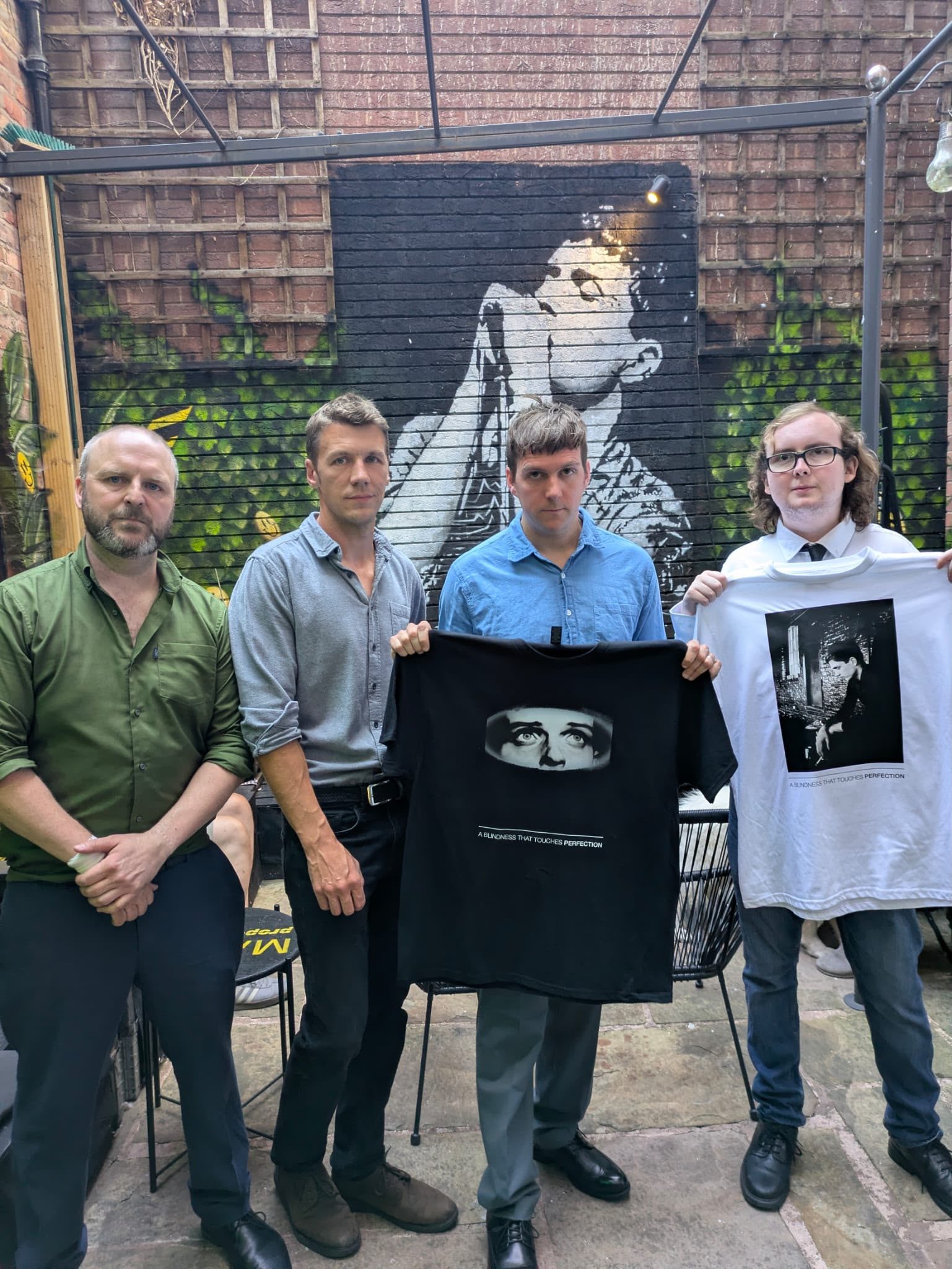 A group holding Ian Curtis tribute T-shirts in the Proper Sound courtyard